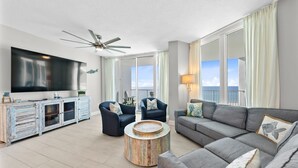 Een moderne woonkamer met een flatscreen televisie, twee fauteuils, een bank, een salontafel en een plafondventilator.