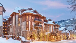 A large, multi-story lodge with a stone facade and wooden balconies, surrounded by snow-covered trees and a mountainous backdrop. - Three Bedroom Residential Suite at The Sebastian Vail (Vail)