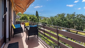 A balcony with wicker furniture and a striped awning, overlooking a green landscape and buildings. - Kostrena Apartment Maja (Kostrena)