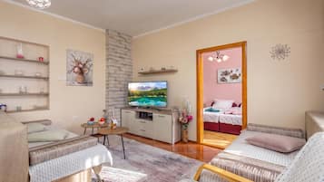Una sala de estar moderna con un televisor de pantalla plana, una zona de comedor con mesa y sillas, y un dormitorio con cama y mesita de noche.