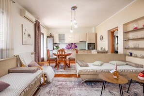 A modern living room with a sofa, a dining table, and a kitchen in the background. - Kostrena Apartment Maja (Kostrena)
