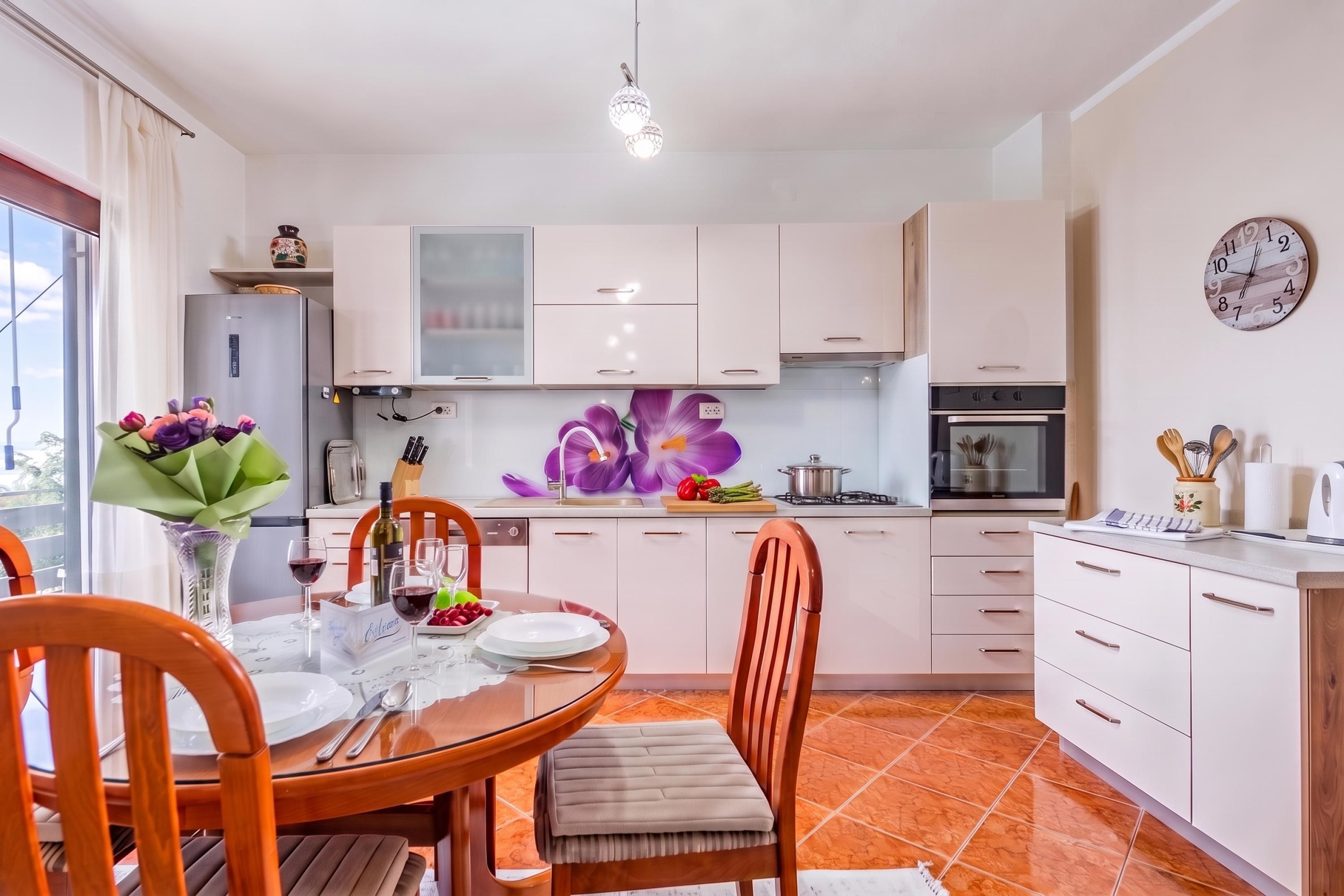 Una cocina moderna con armarios blancos, una mesa de comedor con platos, vasos y un florero.