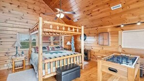 A wooden cabin interior with a four-poster bed, a foosball table, and a ceiling fan. - Majestic 2BD near TOWN! VIEWS + Pool (Pigeon Forge)
