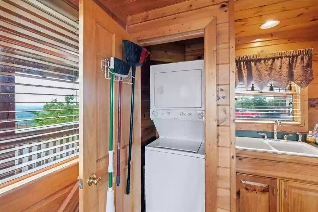 Cocina compacta con lavadora y secadora integradas, armarios de madera y ventana con vistas.