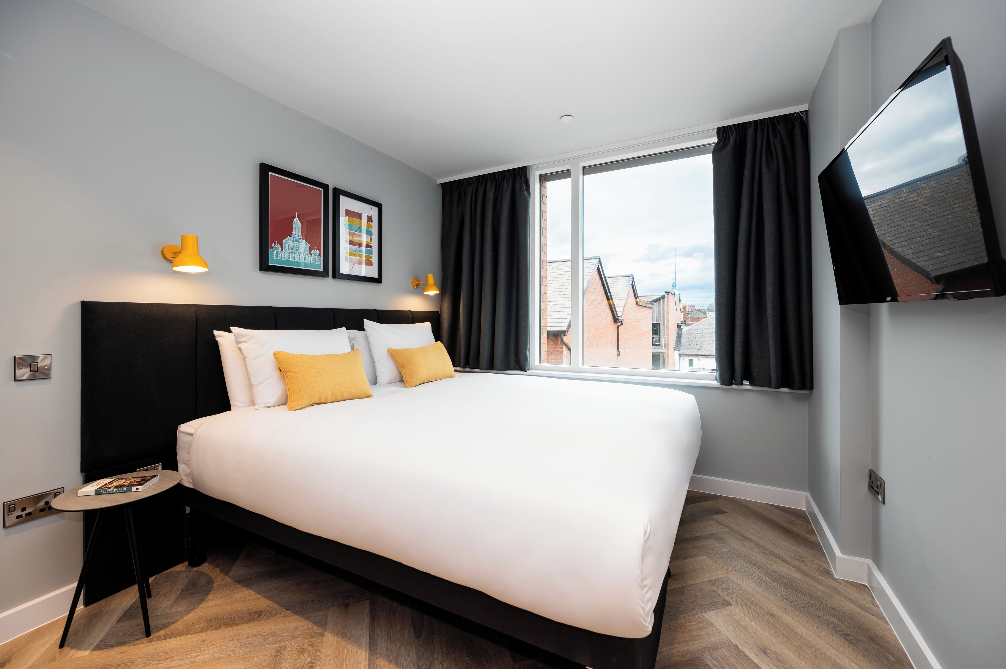 Habitación de hotel moderna con una cama grande, dos lámparas de pared, un televisor de pantalla plana y un ventanal con cortinas.