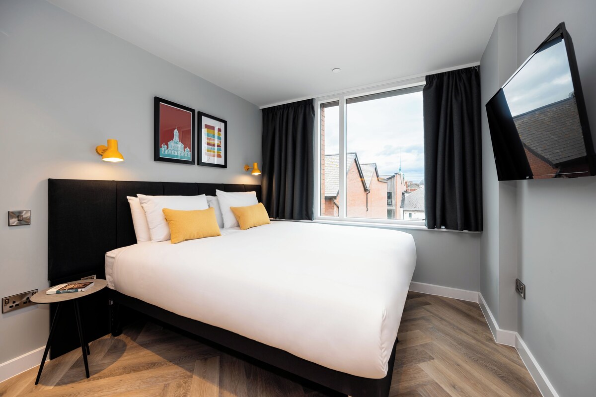 A modern hotel room with a large bed, a flat-screen TV, and a window with curtains.