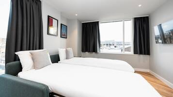A modern hotel room with two beds, large windows, and a city view.