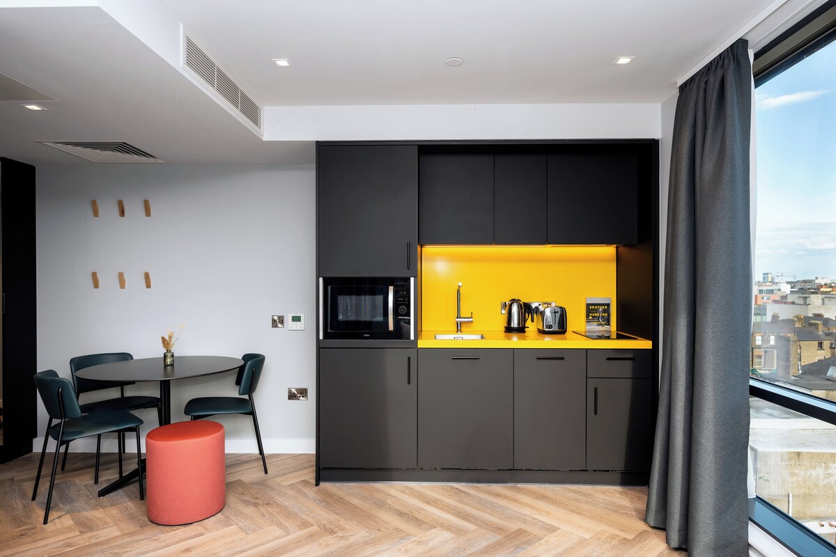 A modern kitchen with black cabinets, a yellow countertop, and a dining area with a round table and chairs.