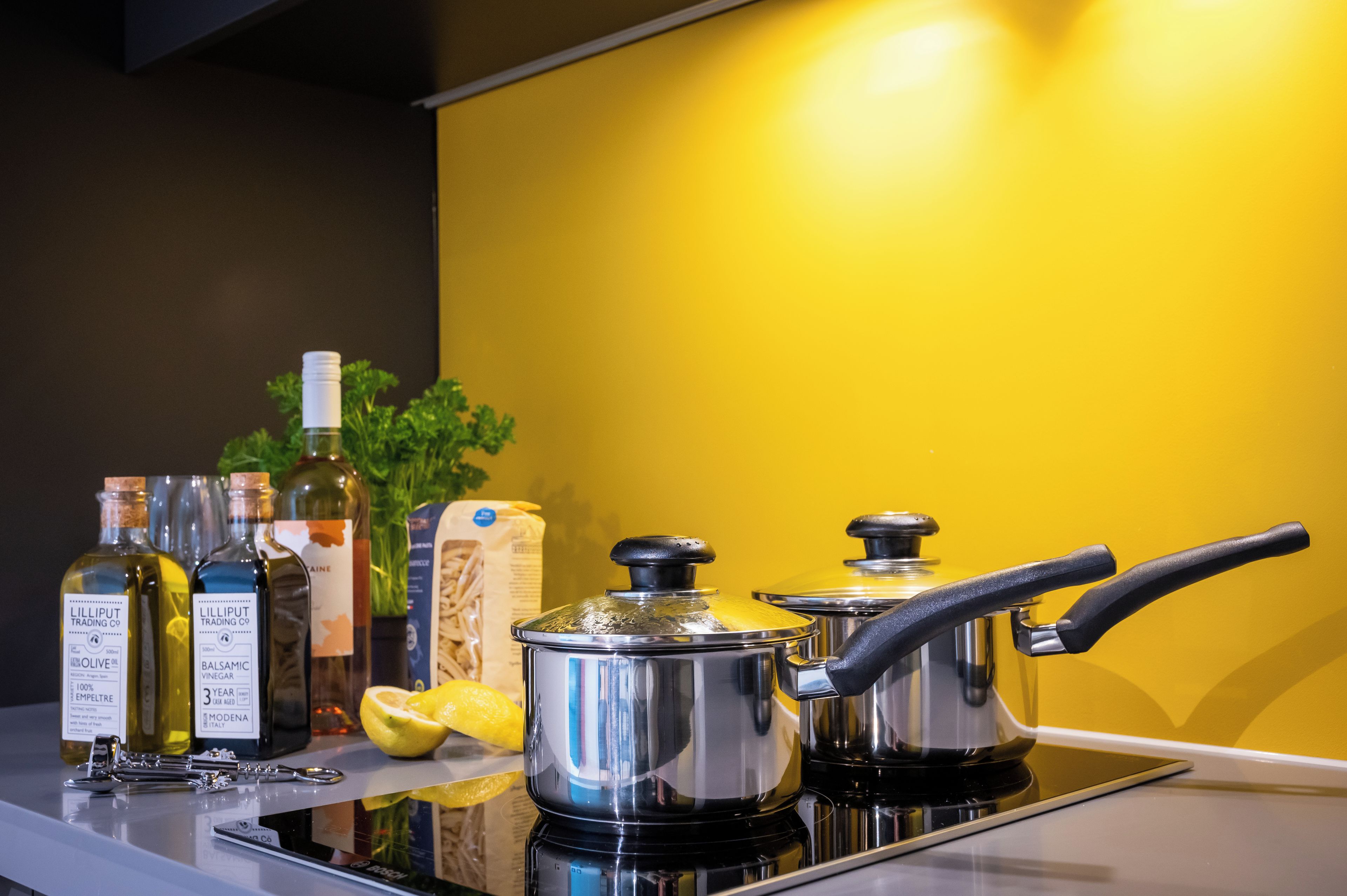 A kitchen counter with cooking pots, bottles of olive oil, balsamic vinegar, and a lemon.