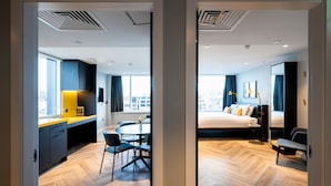 A modern hotel room with a wooden floor, a dining area with a table and chairs, a bed with a black headboard, and a large window with curtains. - Staycity Aparthotels, Dublin, City Centre (Dublin)