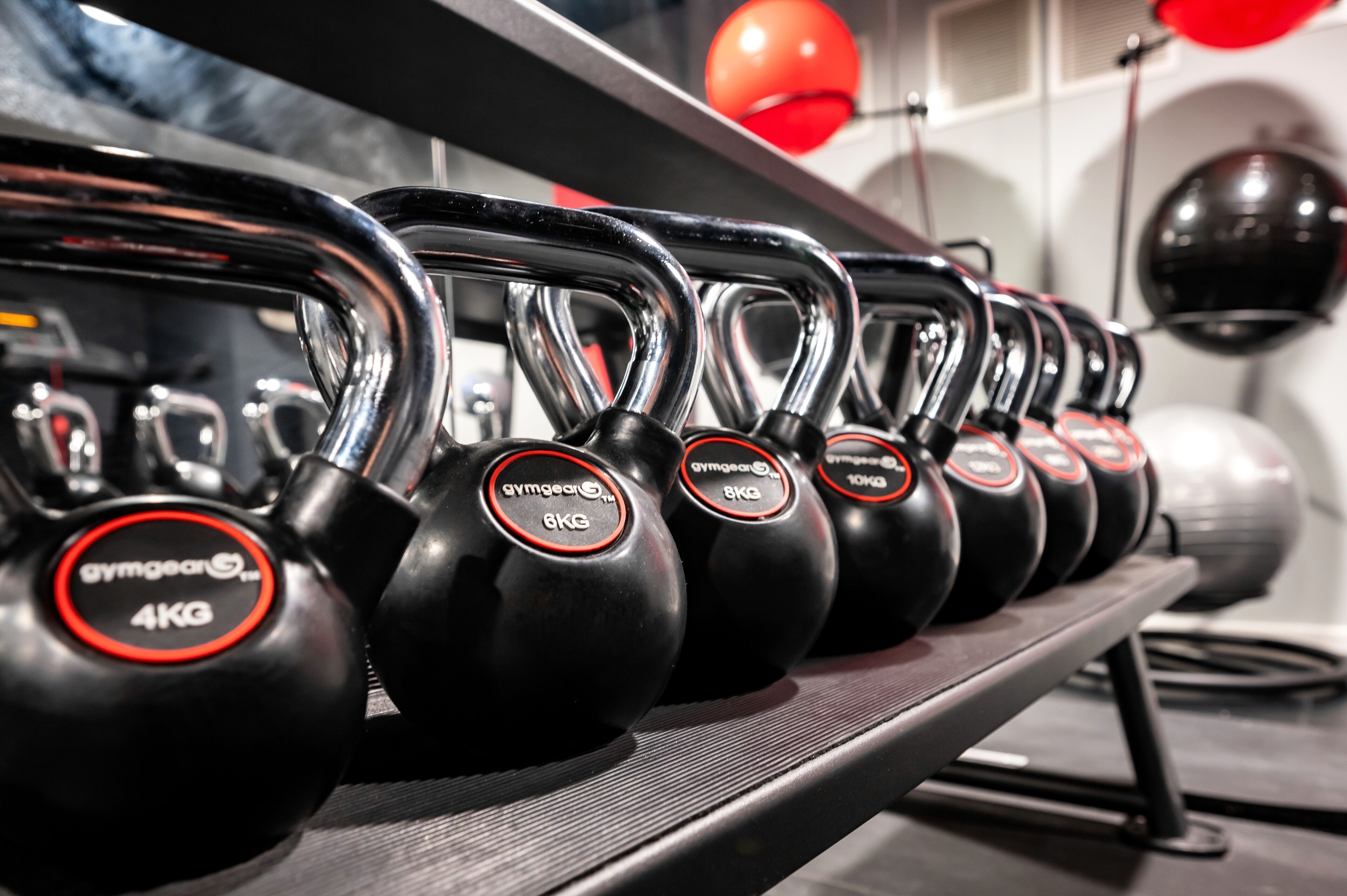 Una fila de equipo de gimnasio, incluyendo kettelbells y una pelota medicinal, en un estante.