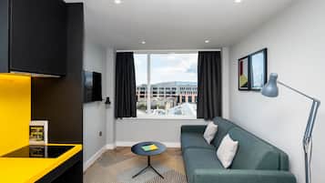 Una habitación de hotel moderna con un sofá verde, una mesita redonda, un televisor negro y una ventana con cortinas.