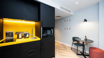 Una cocina moderna con armarios negros, una encimera amarilla y un microondas. Hay una pequeña mesa con una silla y un reposapiés rojo.