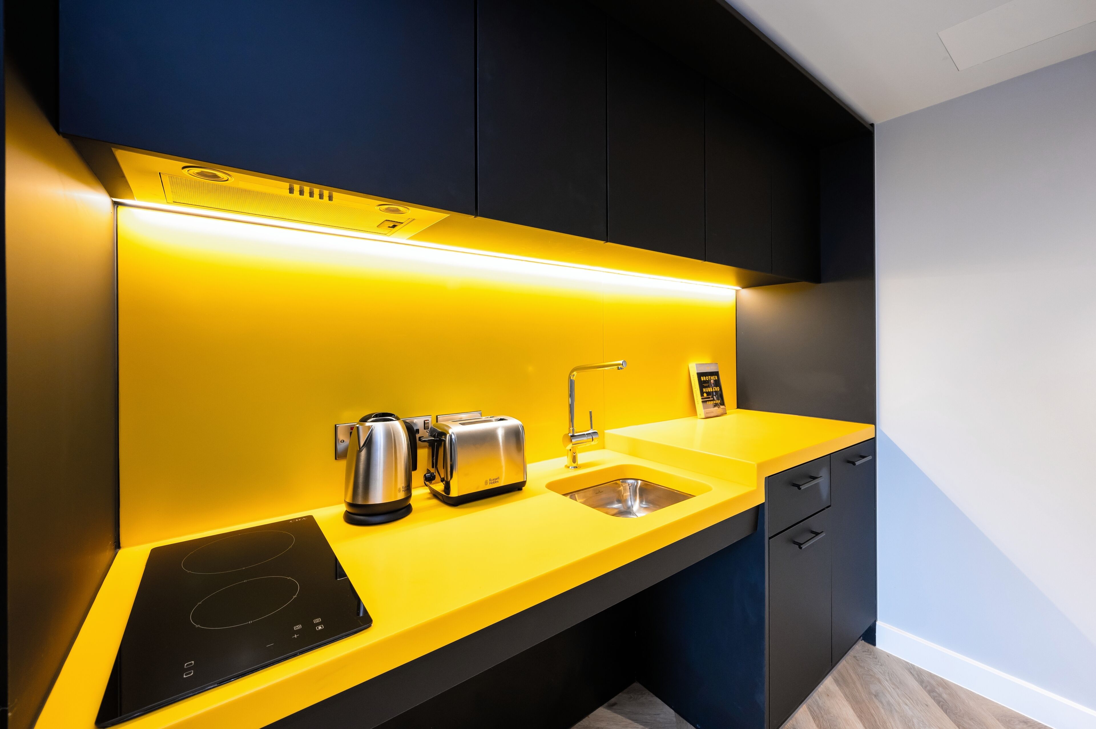 A modern kitchen with a yellow countertop, a built-in induction cooktop, a kettle, a toaster, and a sink.