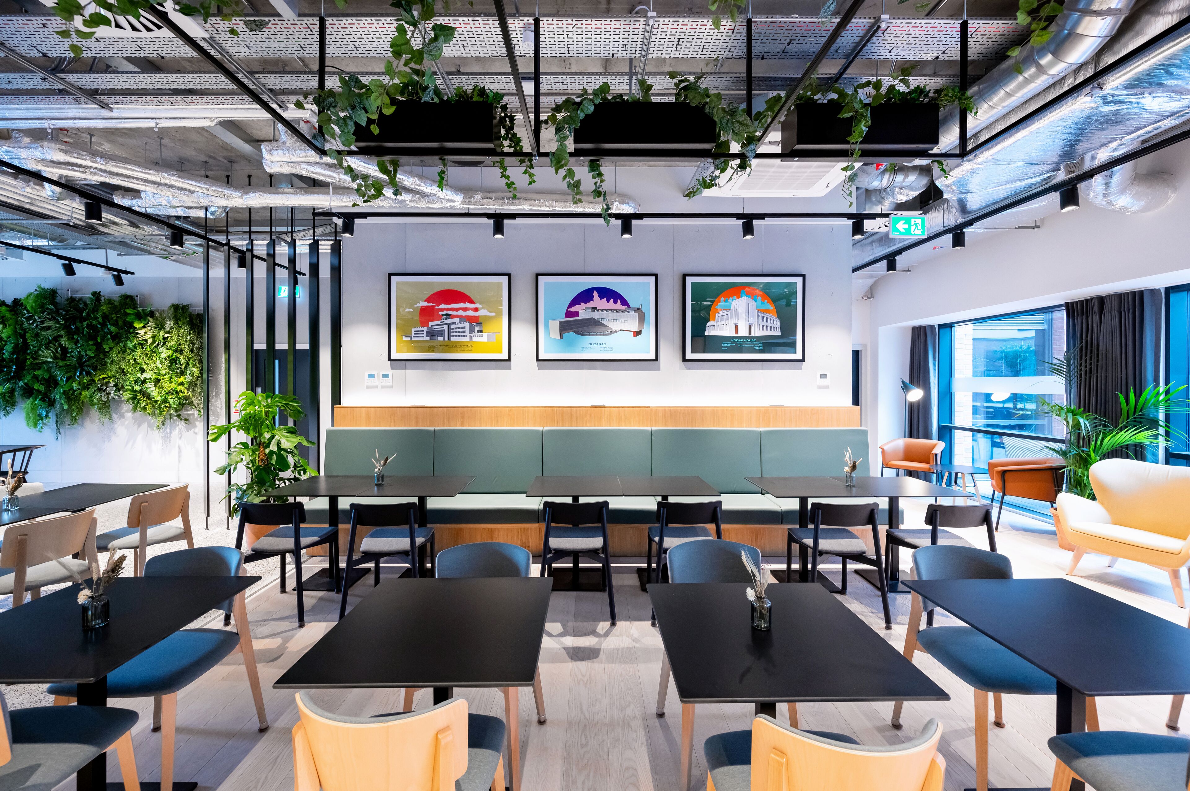 A modern office space with black tables and chairs, green plants, and framed pictures on the wall.