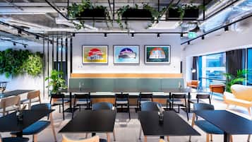 A modern office space with black tables and chairs, green plants, and framed pictures on the wall.