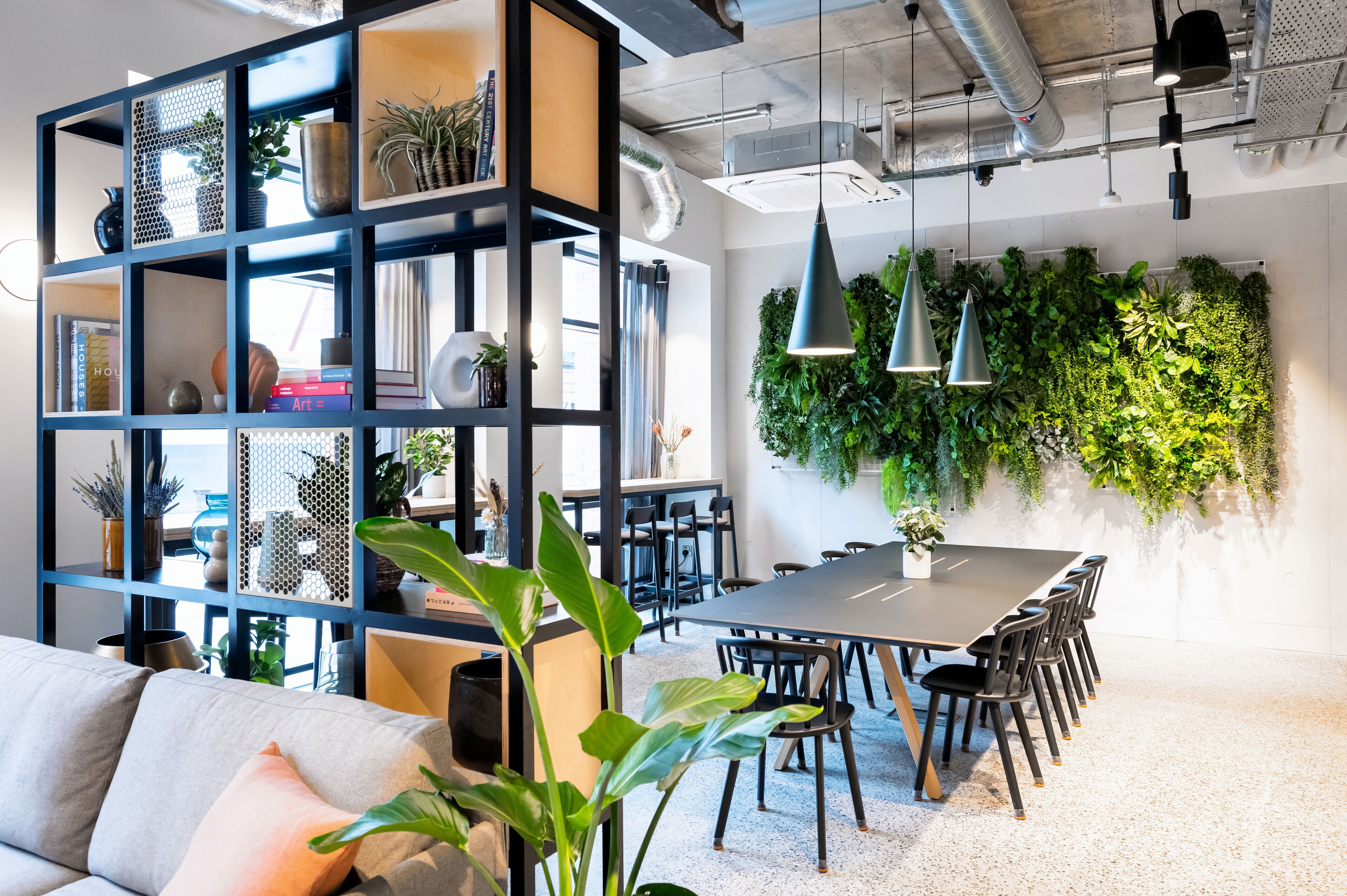 A modern office space with a large bookshelf, a dining table with chairs, and a green wall with plants.