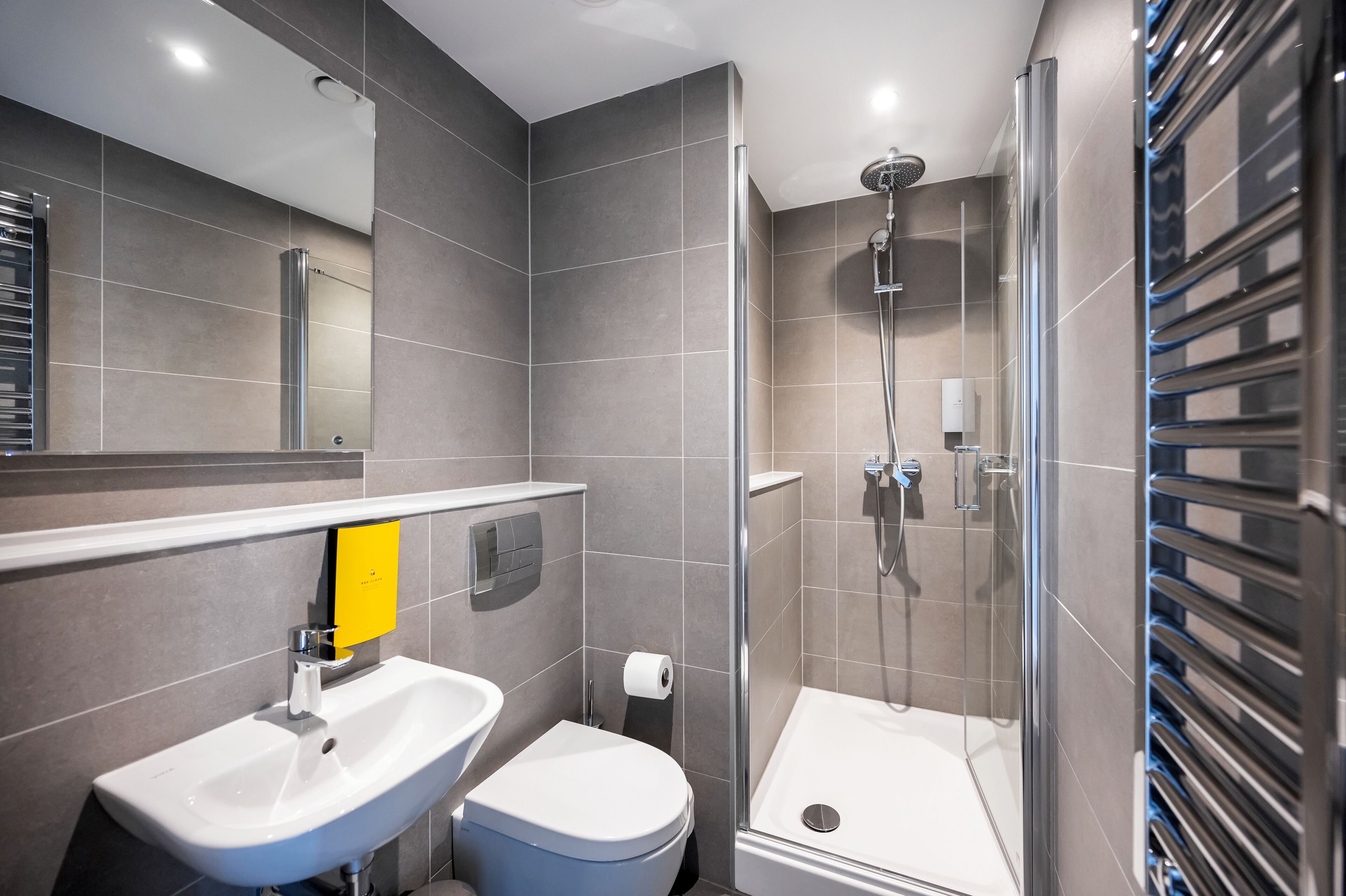 Et moderne badeværelse med et glasafskærmet brusebad, en hvid vask og et toilet.