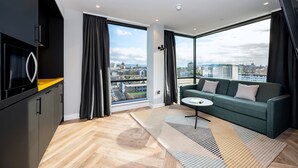 A modern living room with a sofa, a coffee table, and a view of the city through large windows. - Staycity Aparthotels, Dublin, City Centre (Dublin)
