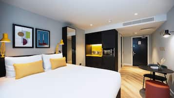 A modern hotel room with a large bed, a desk, and a kitchenette.
