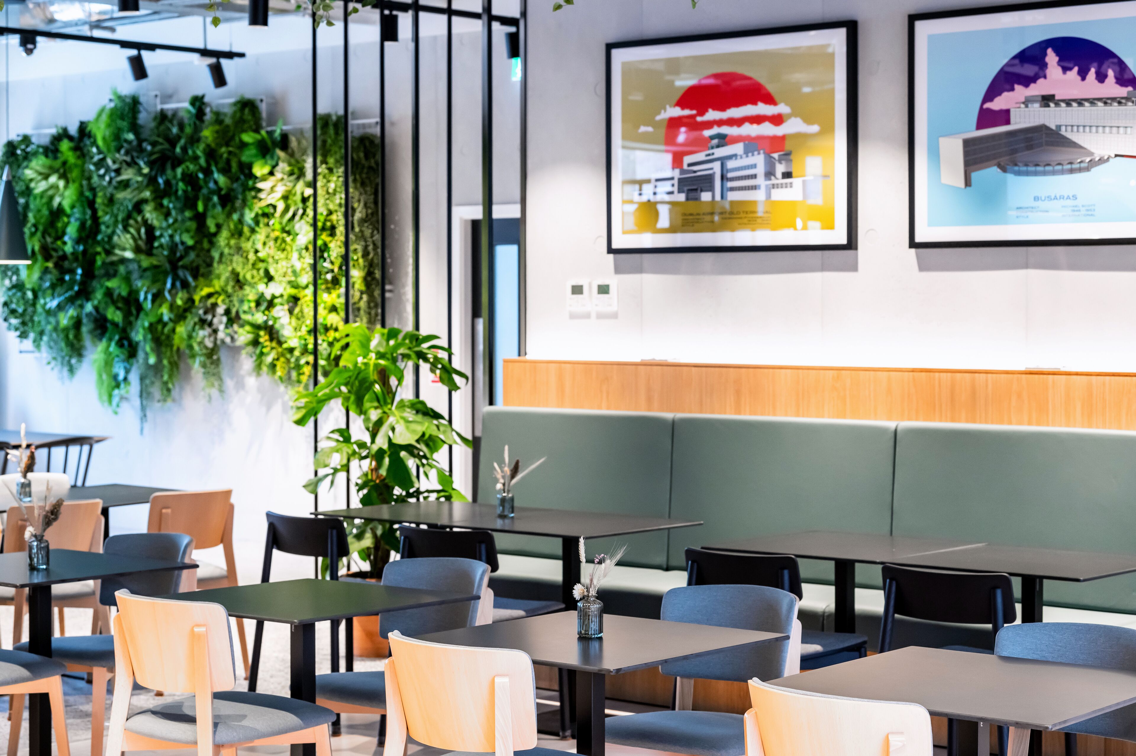 Un restaurant modern amb parets verdes, diverses zones d'aixoplugament i quadres penjats a les parets.