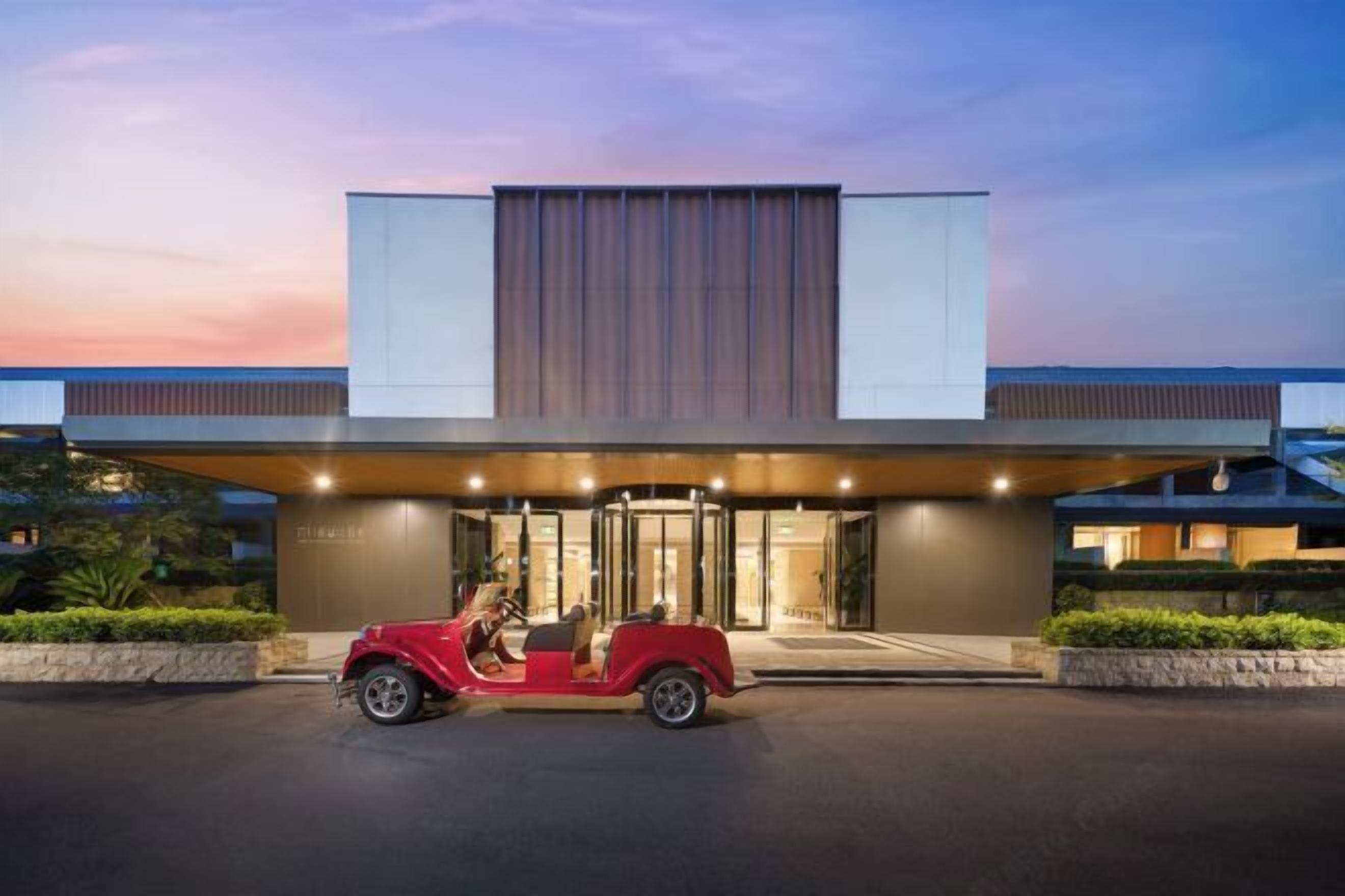 A modern hotel entrance with a red car parked in front.