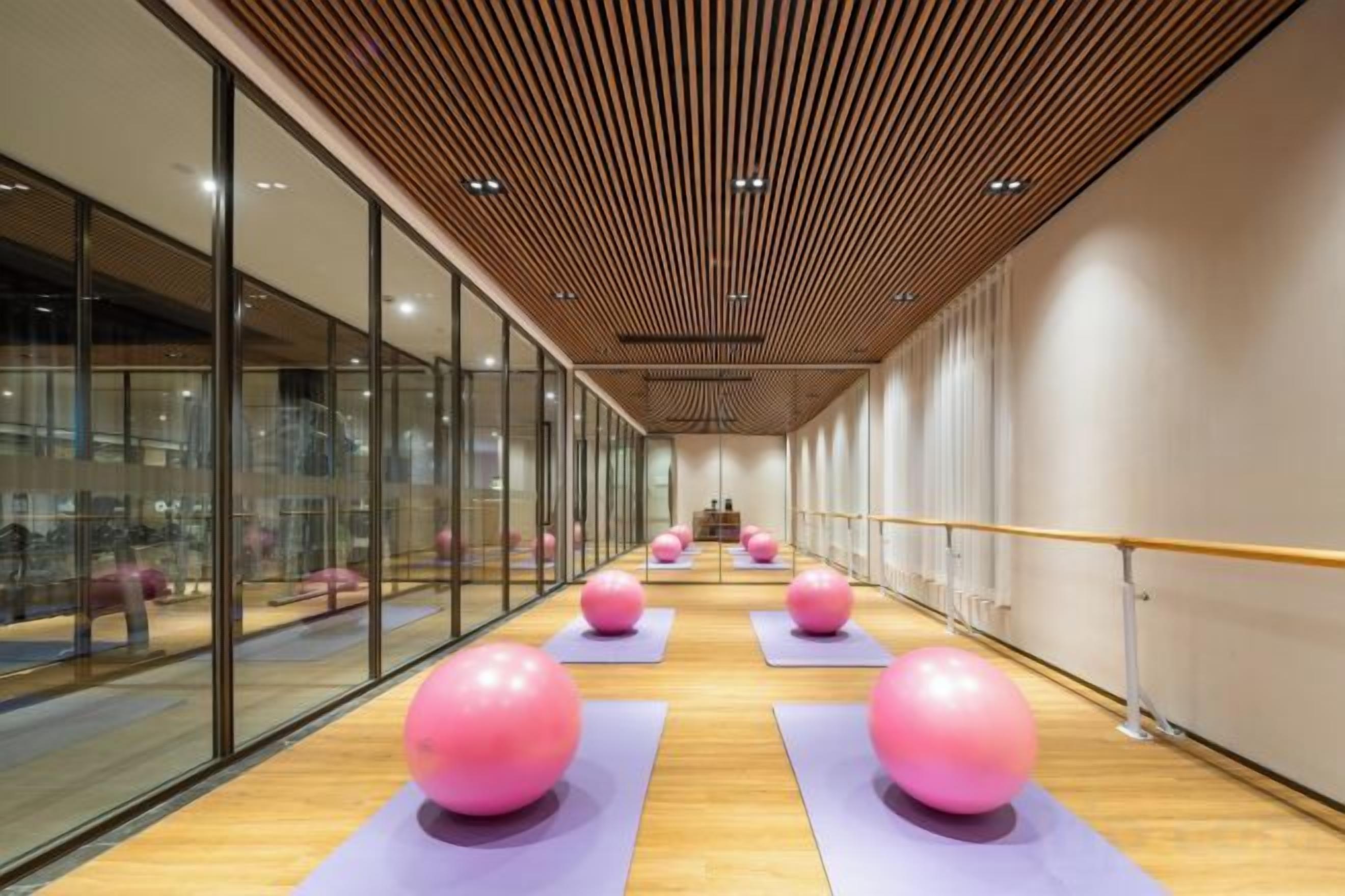 A gym with exercise balls on mats, wooden flooring, and glass walls.
