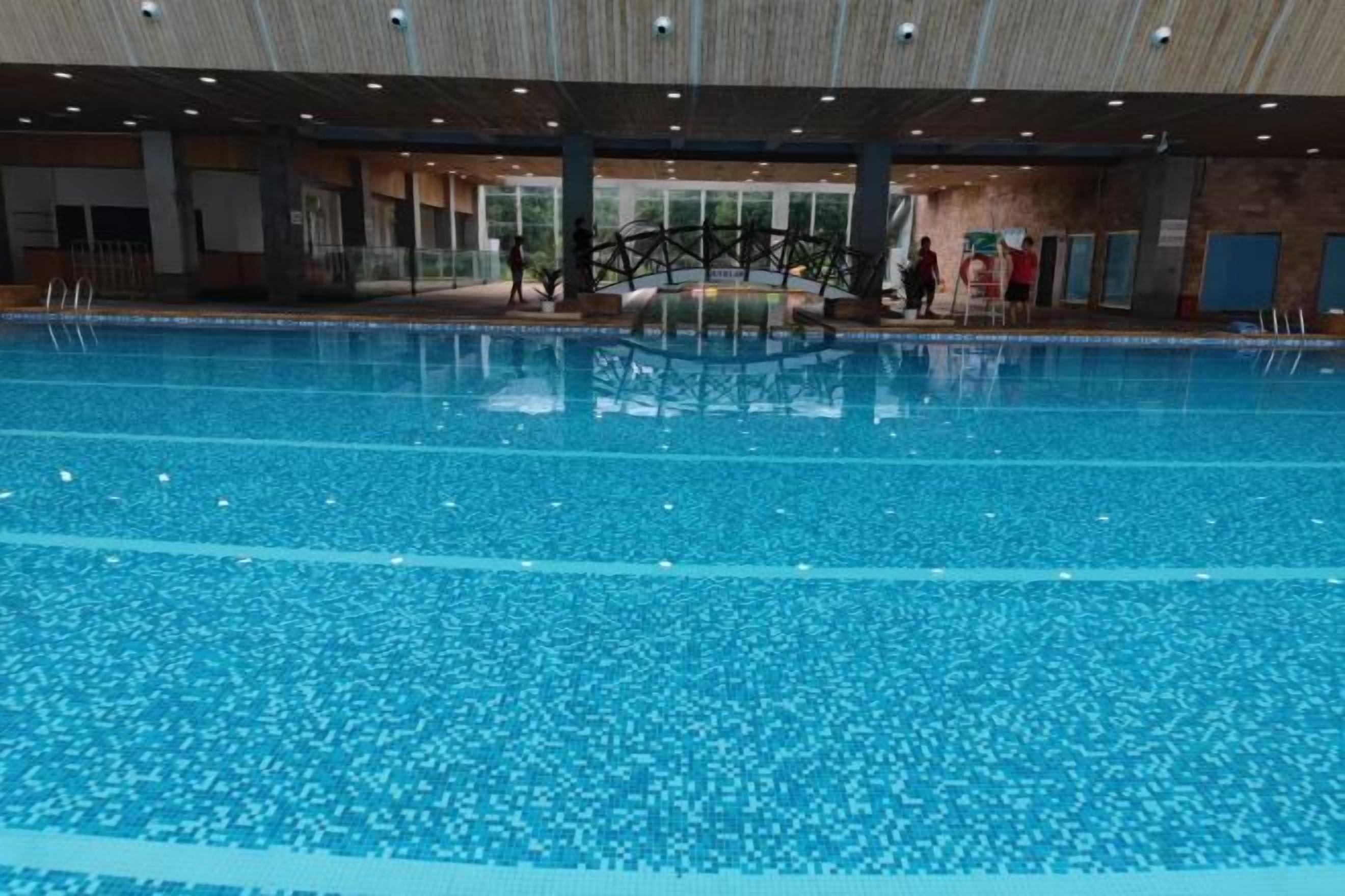 An indoor swimming pool with clear water, surrounded by a covered area with seating and a view of the outdoors.