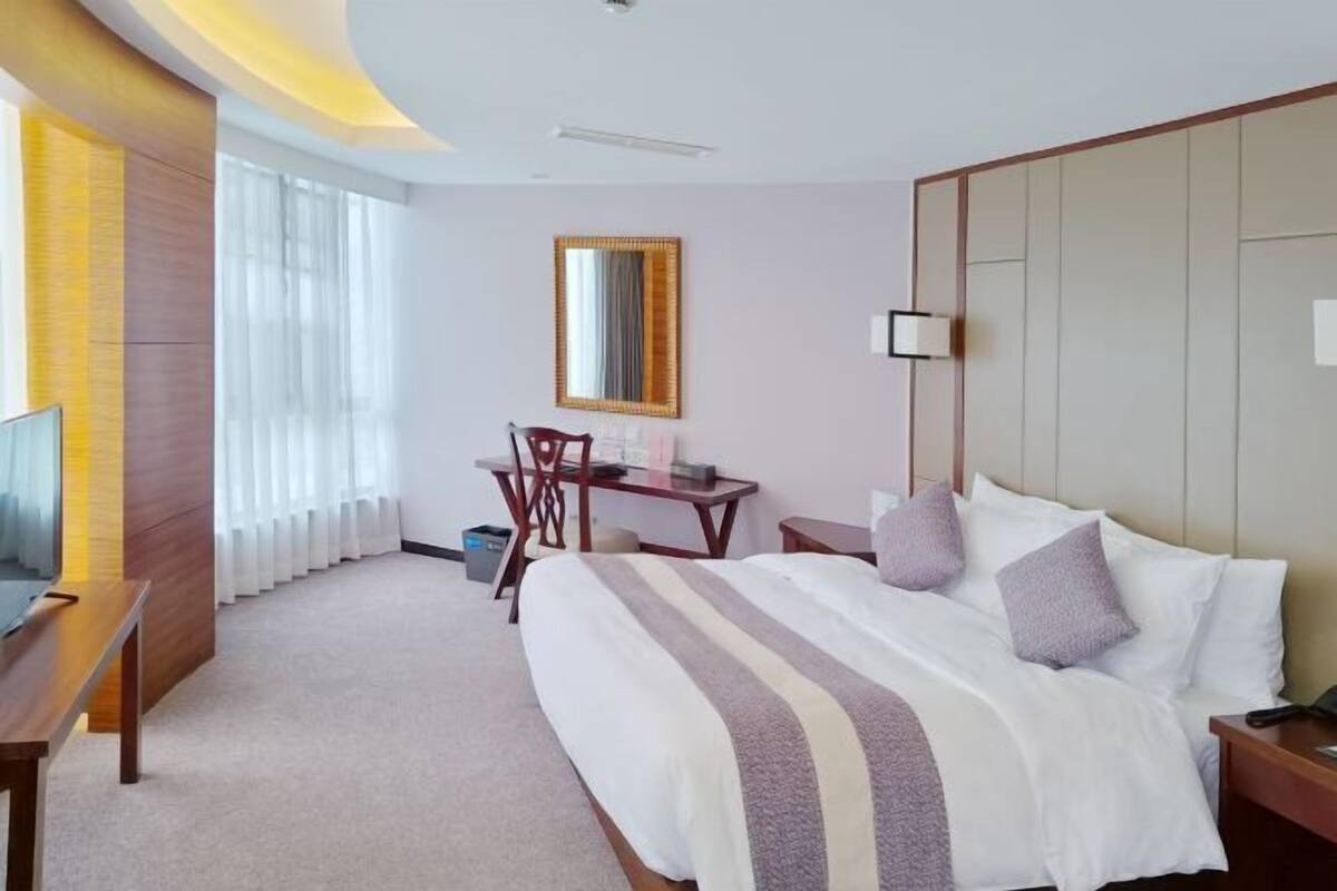 A hotel room with a large bed, a desk, a chair, and a TV.
