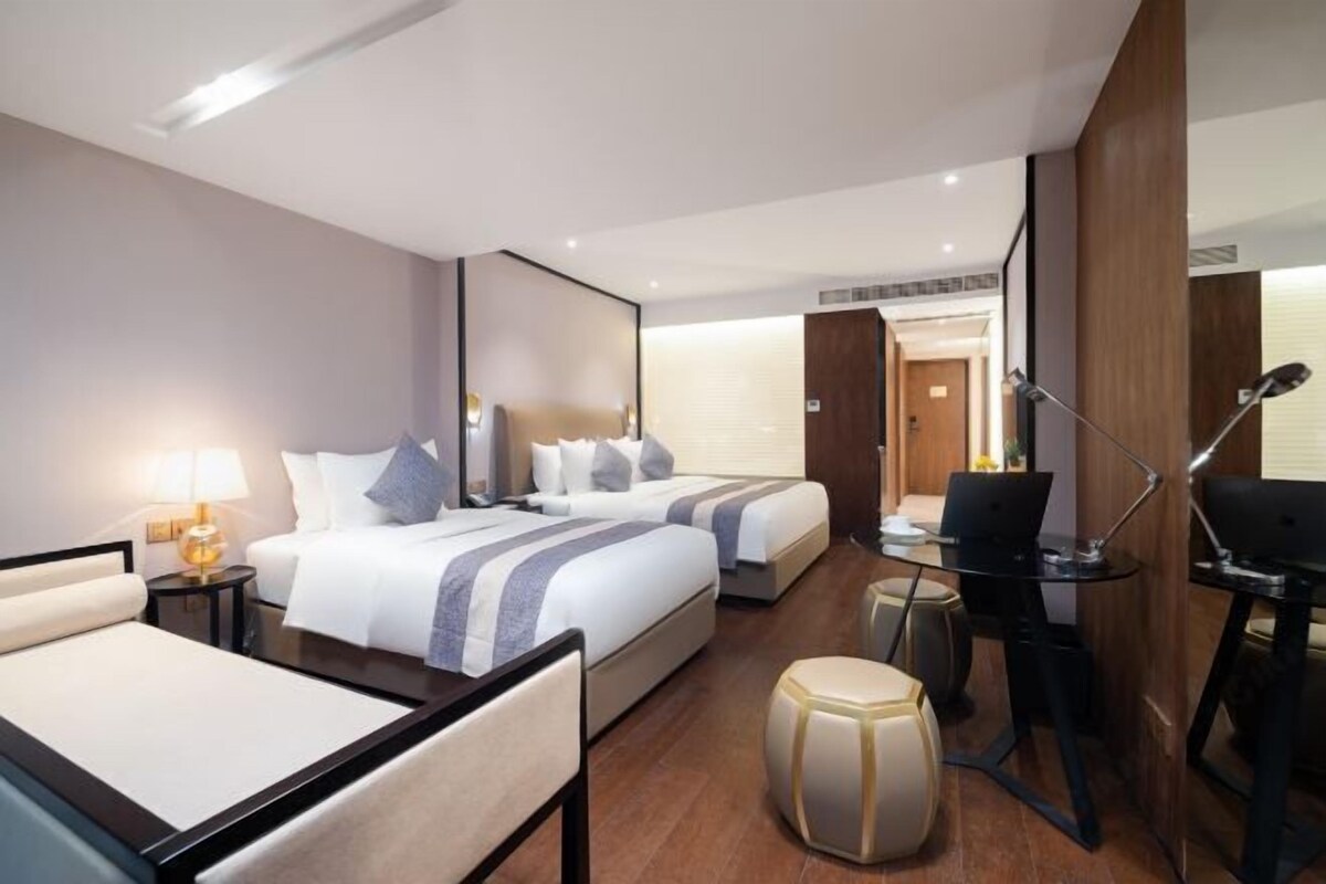 Ein Hotelzimmer mit zwei Betten, einem Schreibtisch, einem Stuhl, einer Lampe und einem kleinen Hocker.