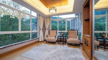 Una habitación amplia con ventanas grandes, techo de madera y dos sillas frente a una pequeña mesa.