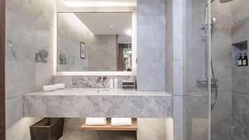Un baño moderno con tocador de mármol, un espejo grande, cabina de ducha y un pequeño estante de madera.