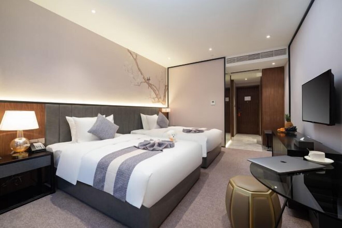 A modern hotel room with two beds, a desk, a TV, and a mirror.