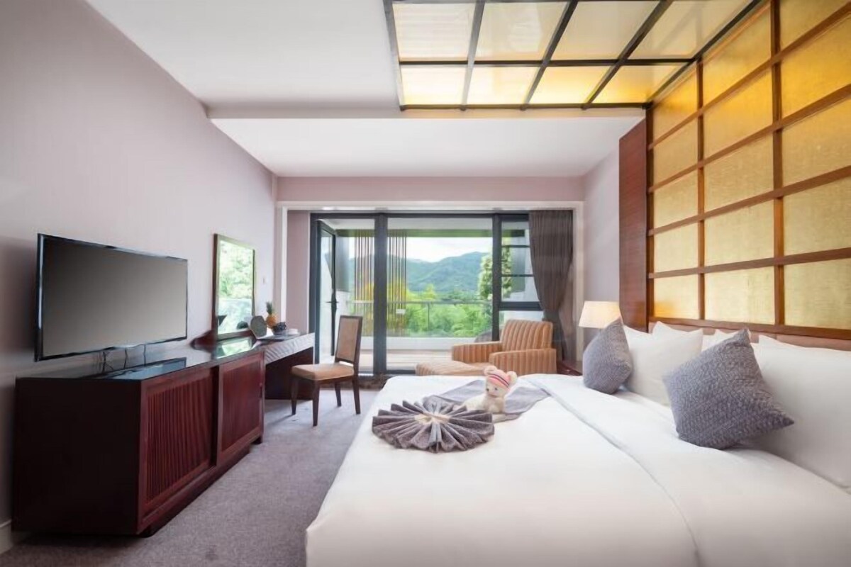 A hotel room with a large bed, a TV, a desk, and a view of the outdoors.