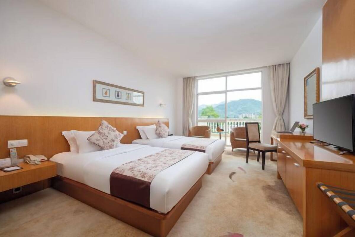 A hotel room with two beds, a desk, a chair, a TV, and a window with a view.