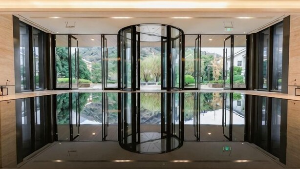 Una puerta giratoria con paneles de vidrio y el reflejo de los alrededores.