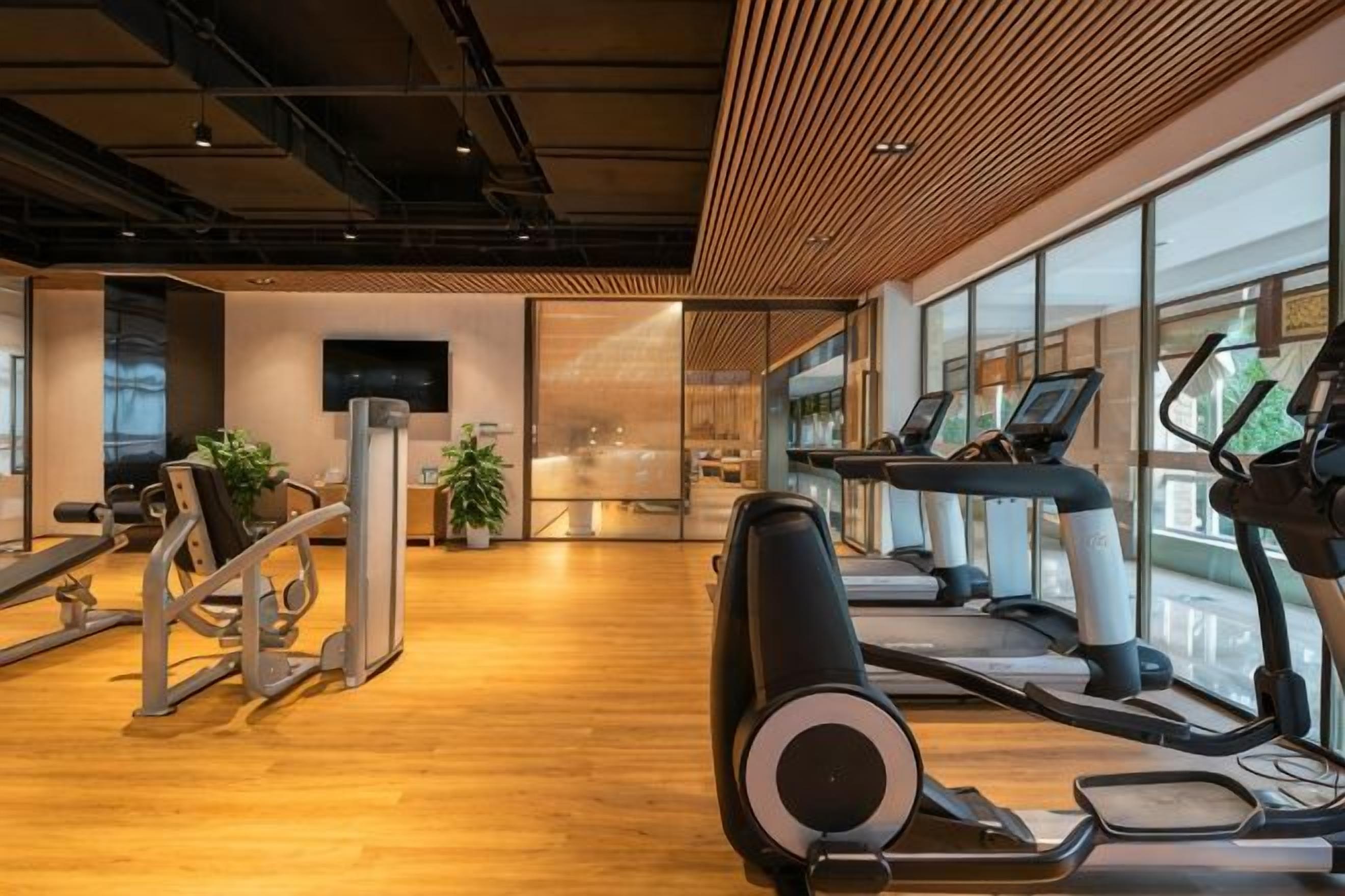 A gym with cardio machines, weight equipment, and large windows.