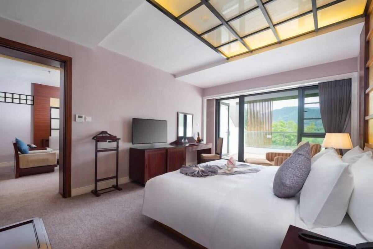 A hotel room with a bed, a television, a desk, and a large window with a view.