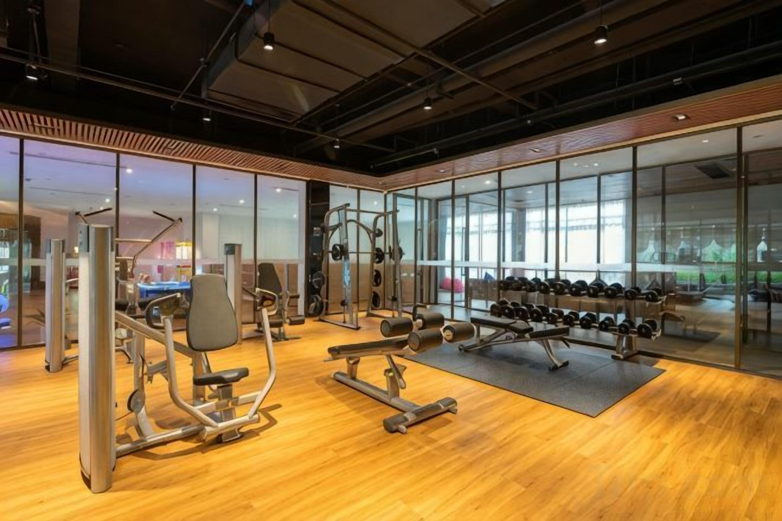 Un gimnasio con diferentes equipos de ejercicio, ventanas amplias y suelo de madera.