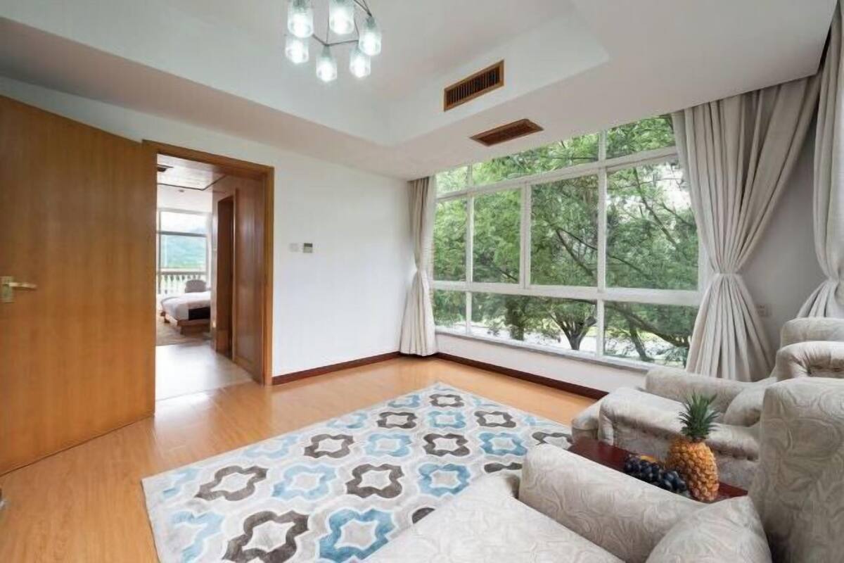 A spacious room with a large window, a patterned rug, and a seating area with a pineapple on a table.