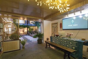 Un área de recepción con un escritorio de madera, una pantalla de televisión y una escalera que lleva a un jardín exterior.