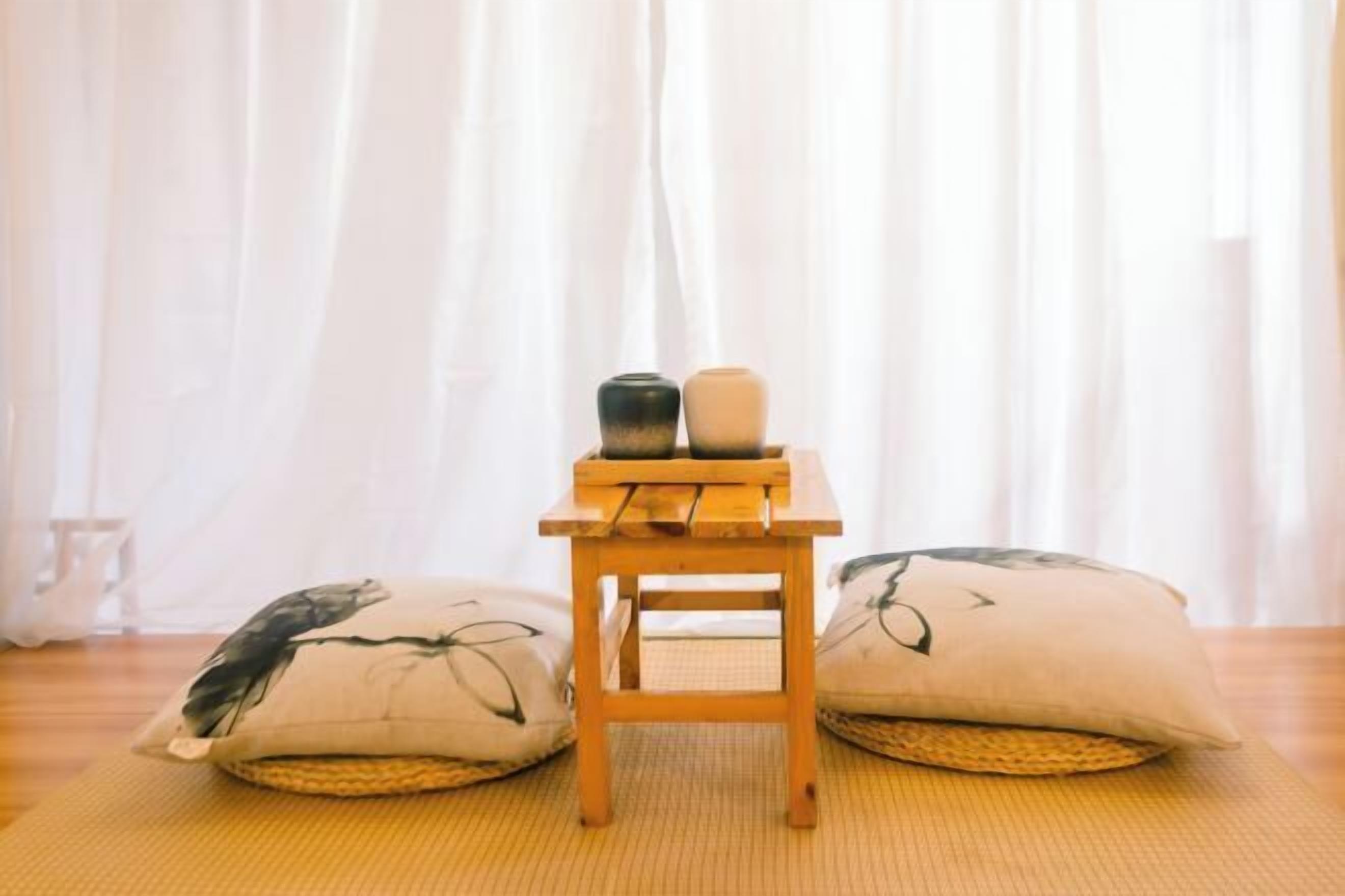 Una habitación con suelo de tatami, una pequeña mesa de madera con dos adornos y dos cojines con motivos naturales.