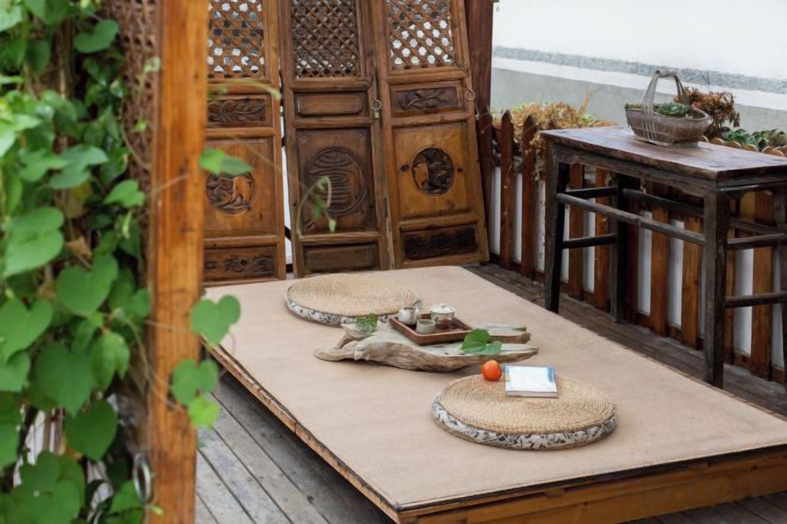 Une terrasse en bois avec une table dressée pour deux personnes, entourée d’une clôture en bois ornée de sculptures complexes.