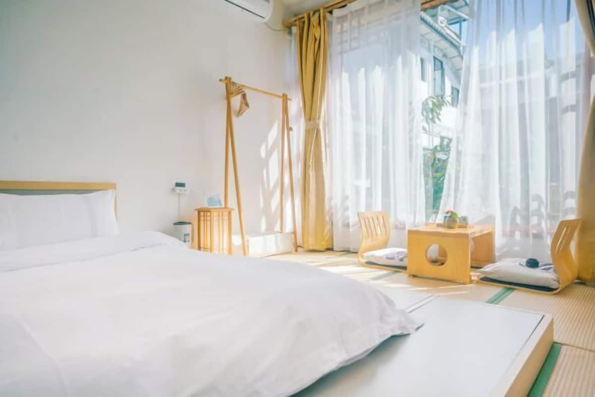 A hotel room with a large bed, a small table, a chair, and a window with curtains.
