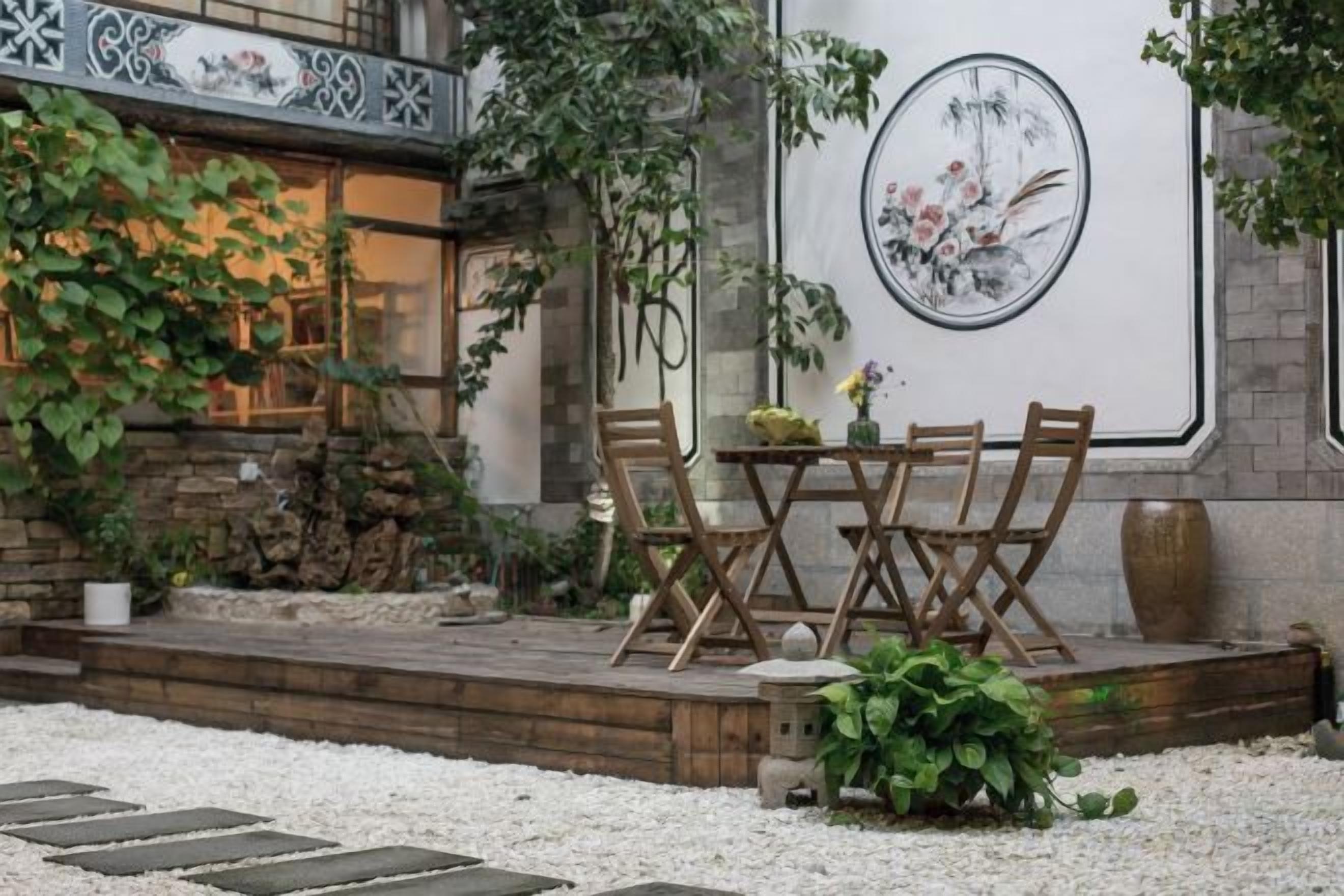 An outdoor seating area with a wooden table and chairs, surrounded by a stone wall and plants.