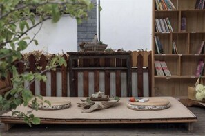 Una mesa de madera con un felpudo tejido, un taburete de madera pequeño y una cesta en una terraza.