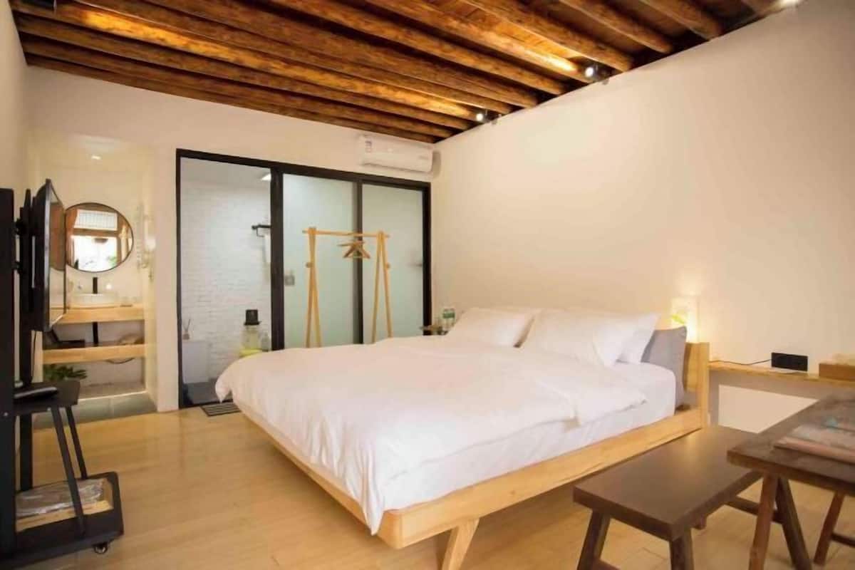 A bedroom with a wooden bed, a desk, a chair, a mirror, and a wardrobe.
