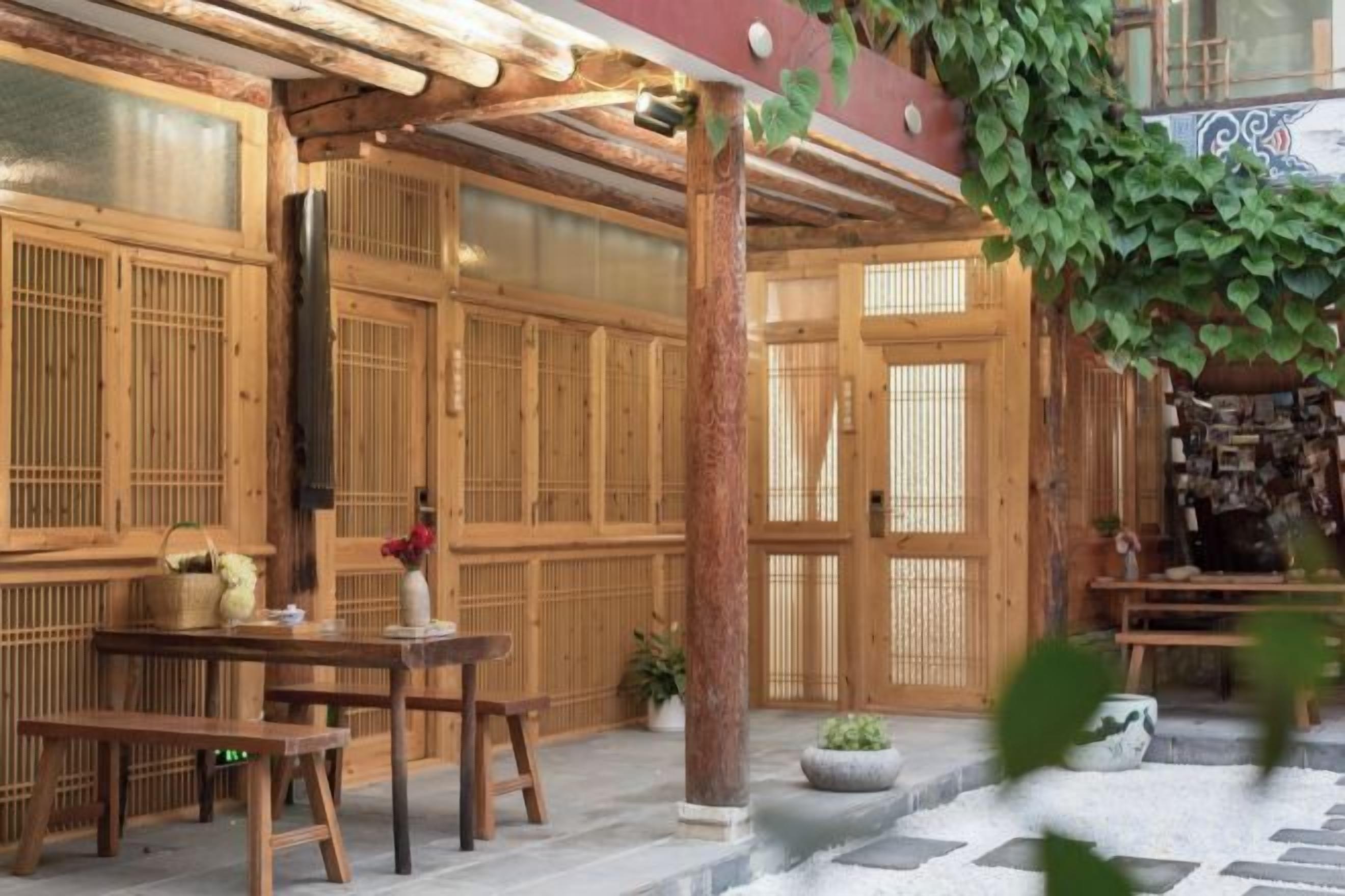 A traditional wooden building with a covered patio area, featuring a table and benches, and a potted plant.
