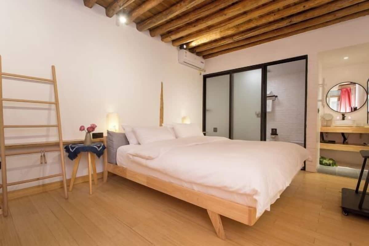 A bedroom with a wooden bed, a ladder, a small table with flowers, and a mirror.