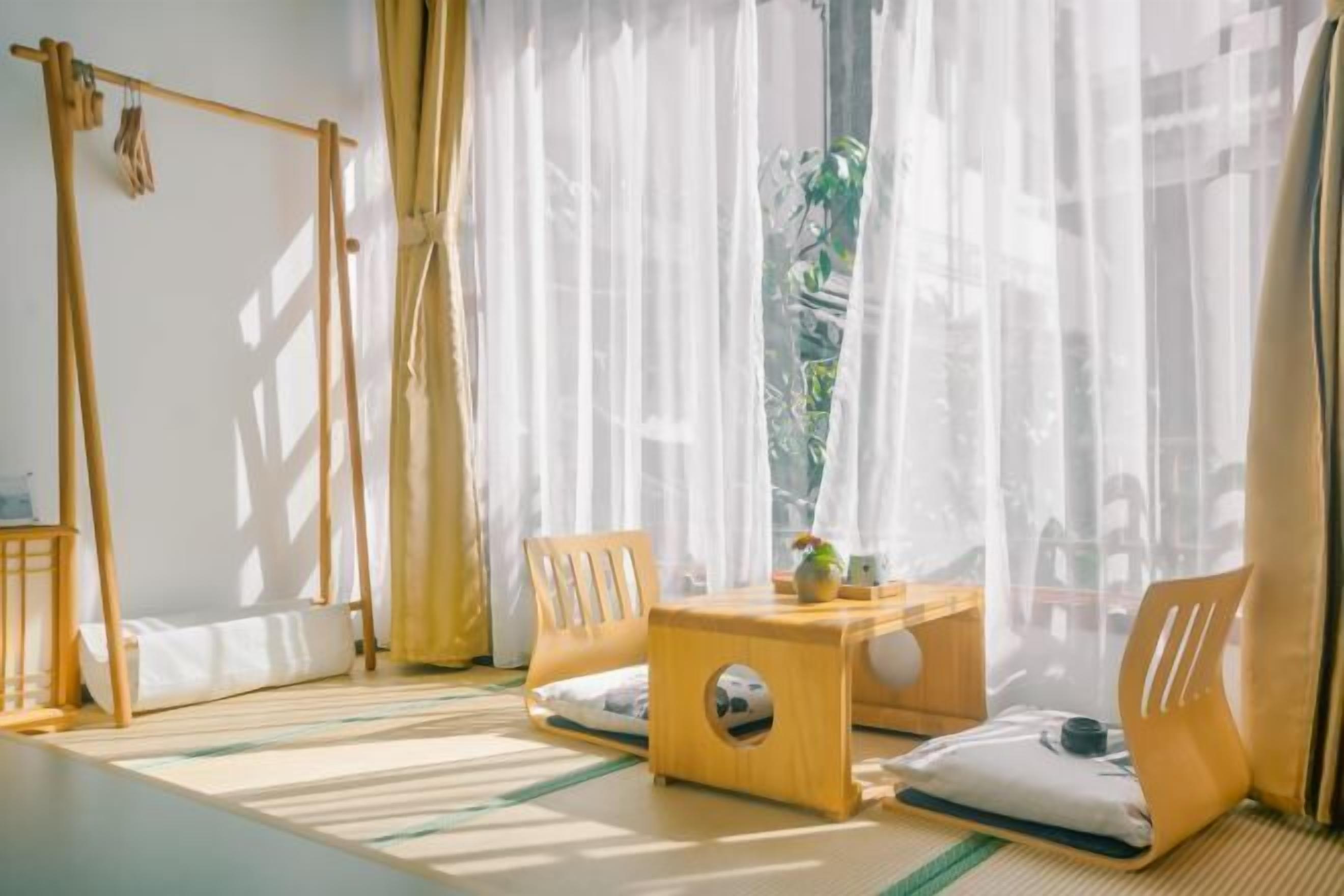 A room with tatami mats, a low wooden table, two chairs, a hanging rack, and sheer curtains.